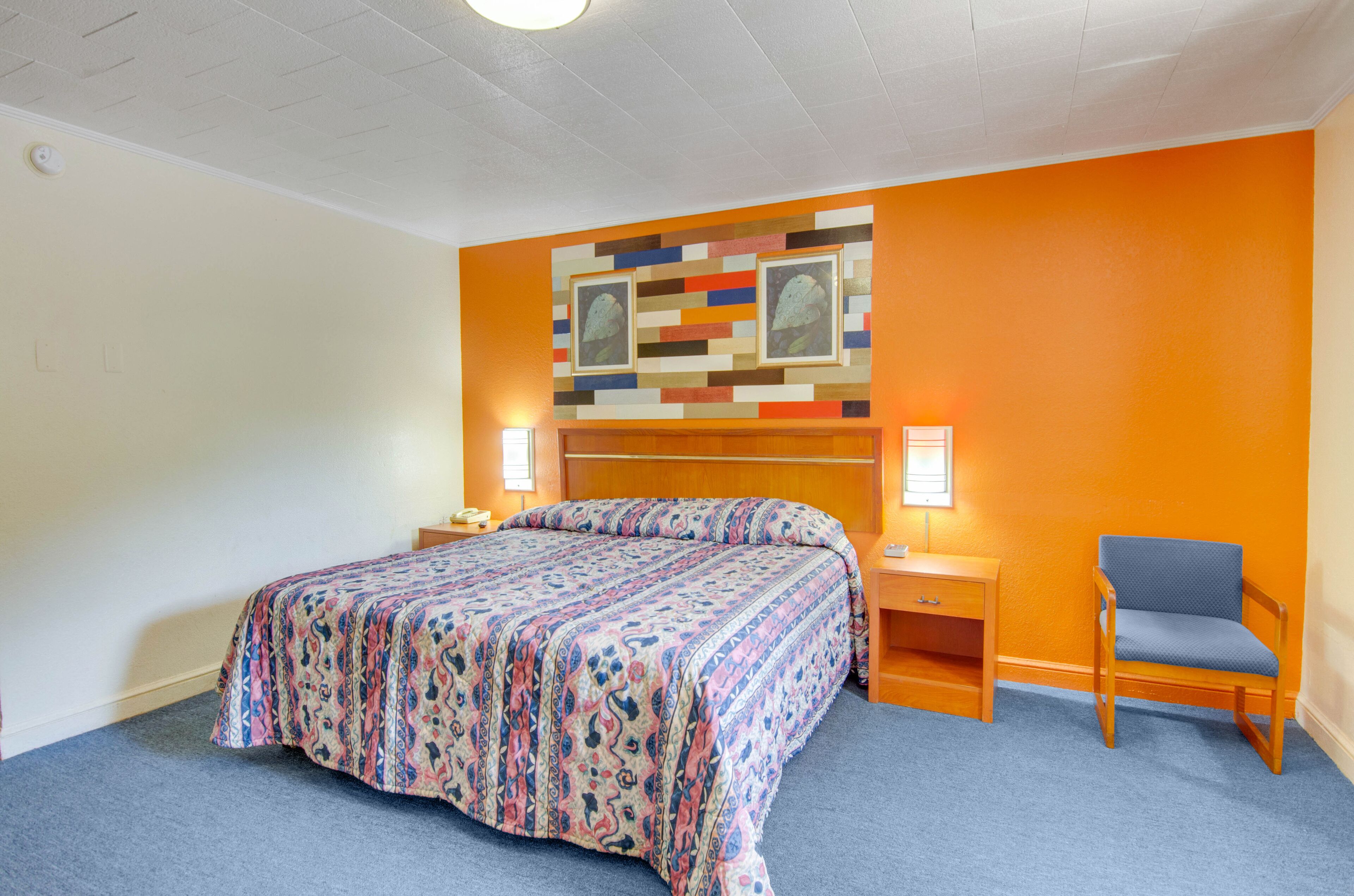 A hotel room with a bed, a nightstand, a chair, and a wall with a colorful pattern.