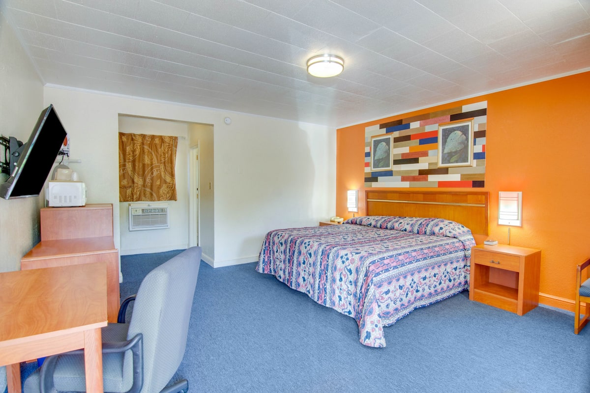 Un dormitorio con cama, escritorio, silla y una pared decorada con una obra de arte colorida.