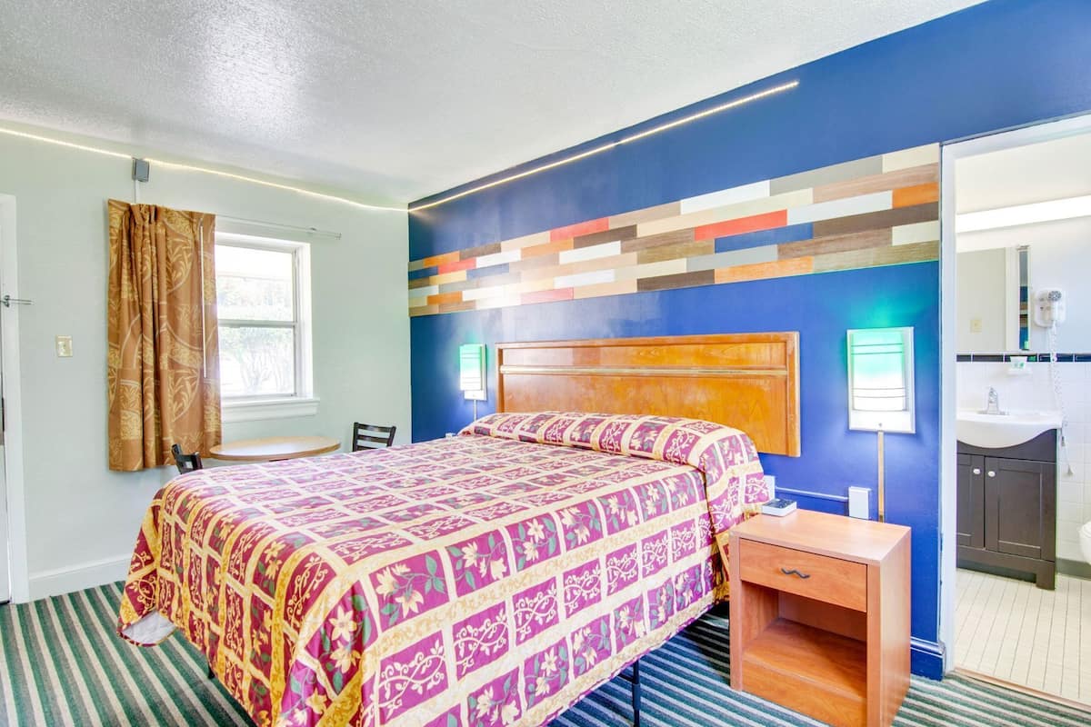 Habitación de hotel con cama, mesita de noche y baño visible a través de una puerta abierta.