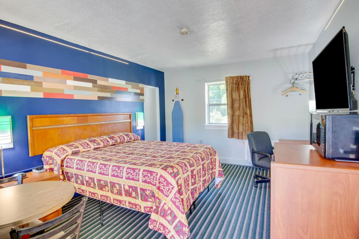 Habitación de hotel con cama, escritorio, silla, televisión y ventana con cortinas.