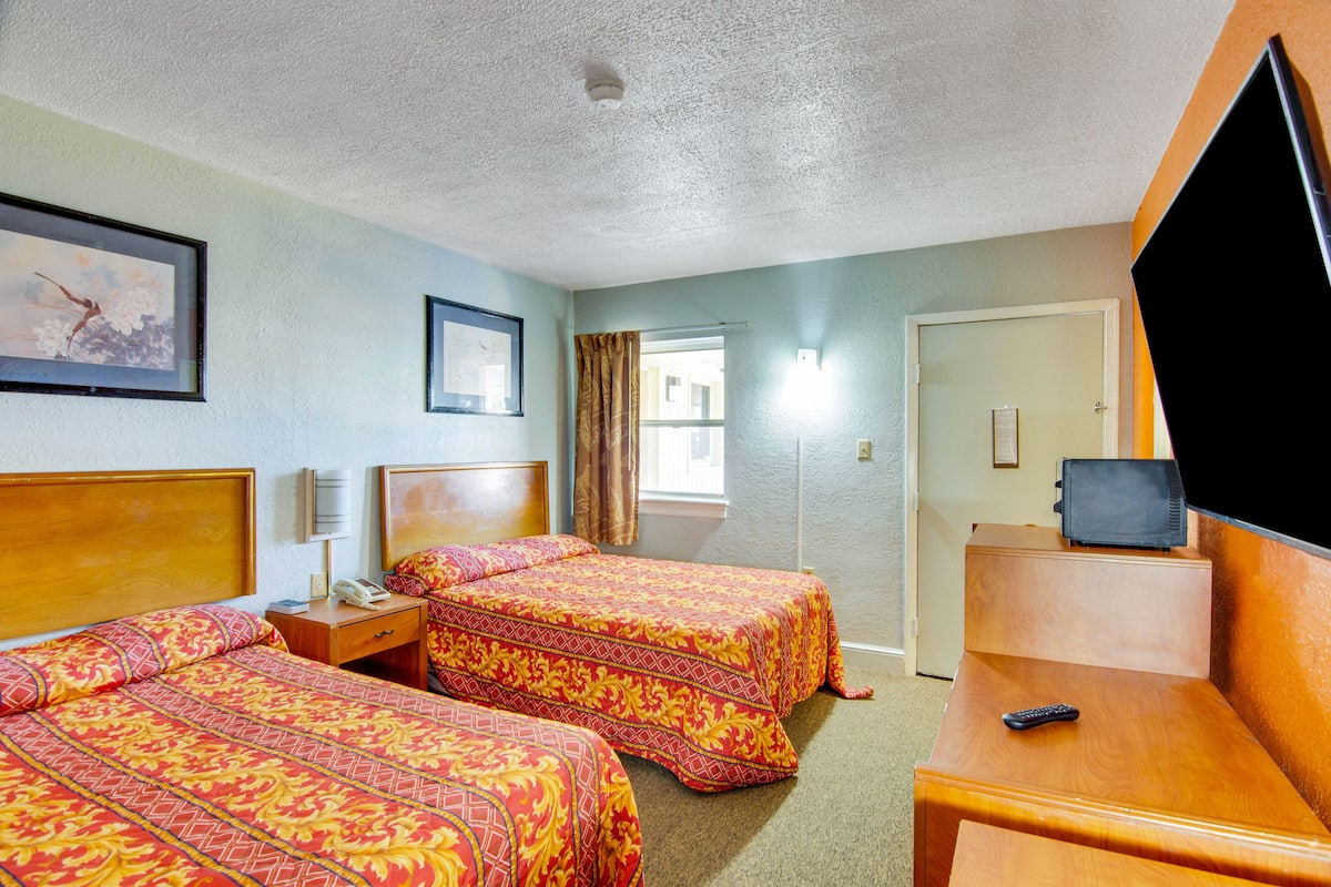 Una habitación de hotel con dos camas, un televisor, un escritorio y una ventana con cortinas.