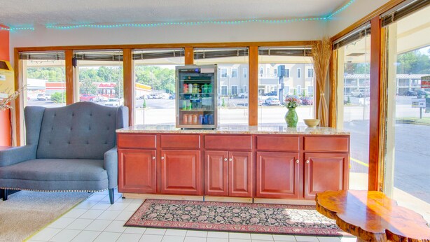 Een kamer met een grijze fauteuil, een houten kast, een klein houten tafeltje en een koelkast.