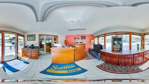 Een receptiegedeelte met een balie, een bank en een vloerkleed met de tekst 'Scottish Inn'.