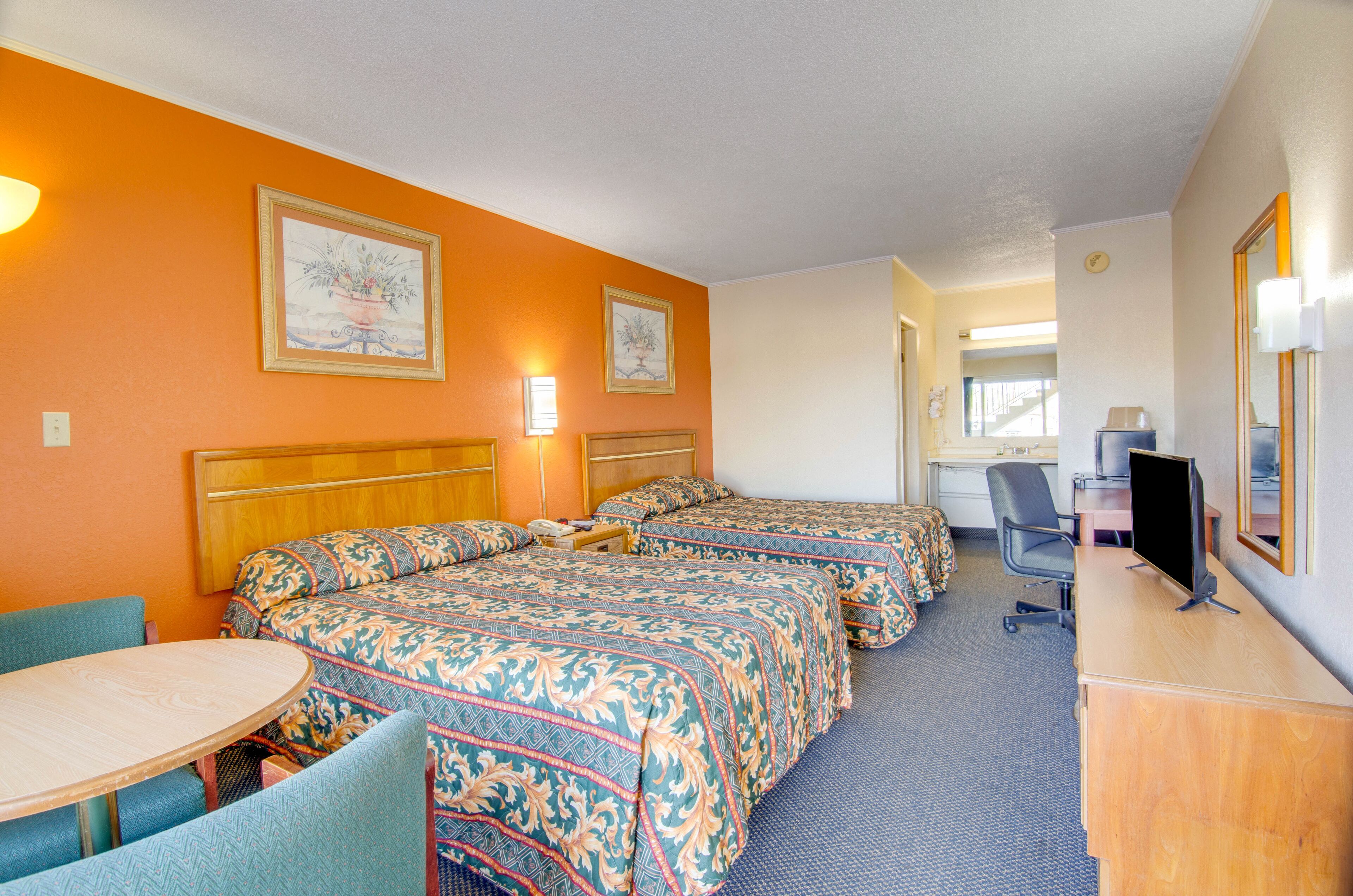 A hotel room with two beds, a desk with a computer, a chair, and a table.