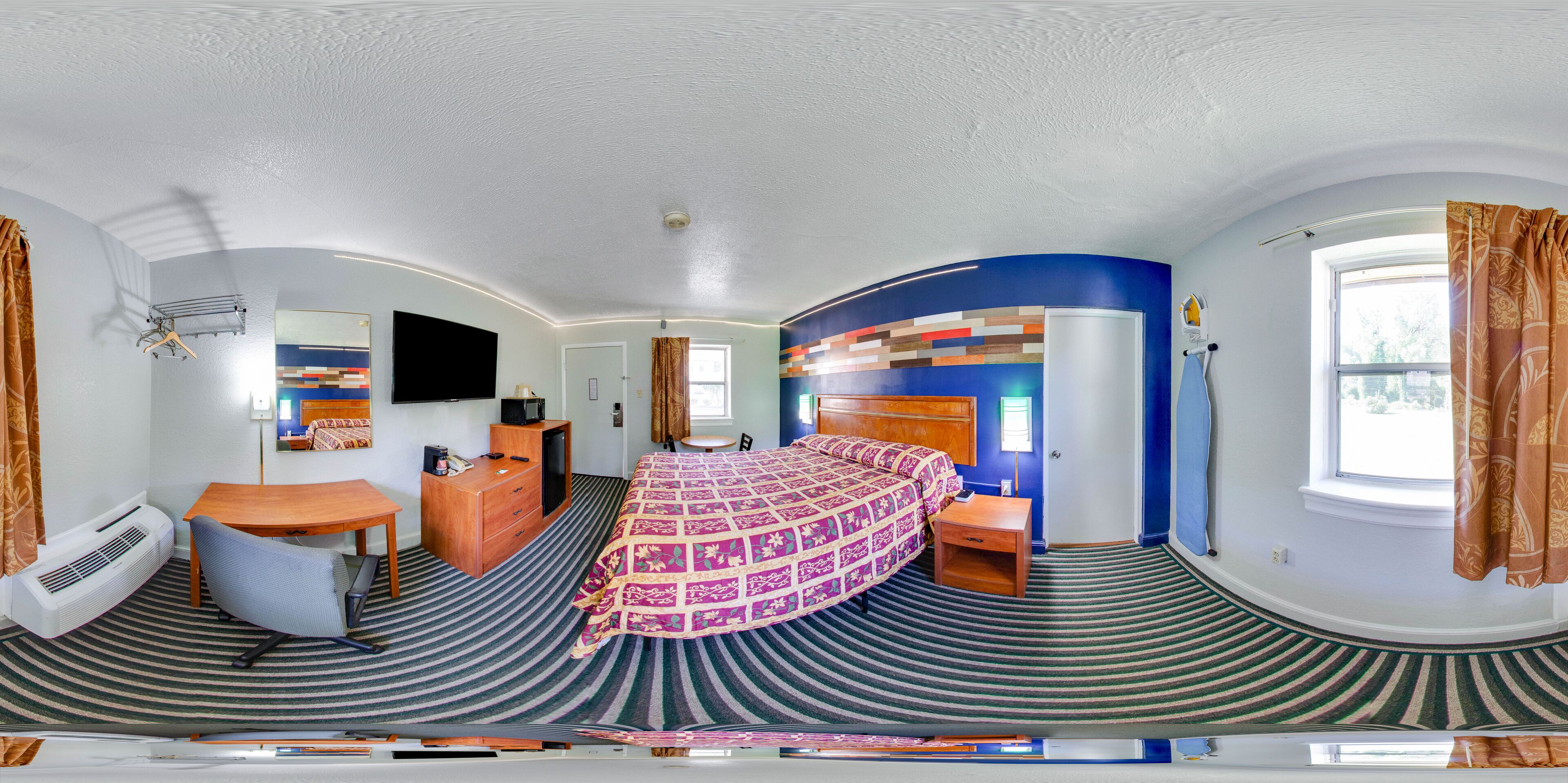 Ett hotellrum med en säng, ett skrivbord, en stol, en tv och ett fönster.