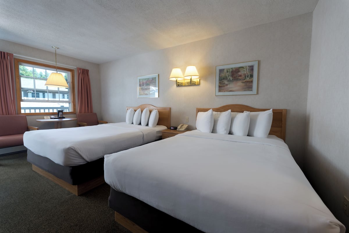 A hotel room with two beds, a sofa, a small table, and a window with curtains.