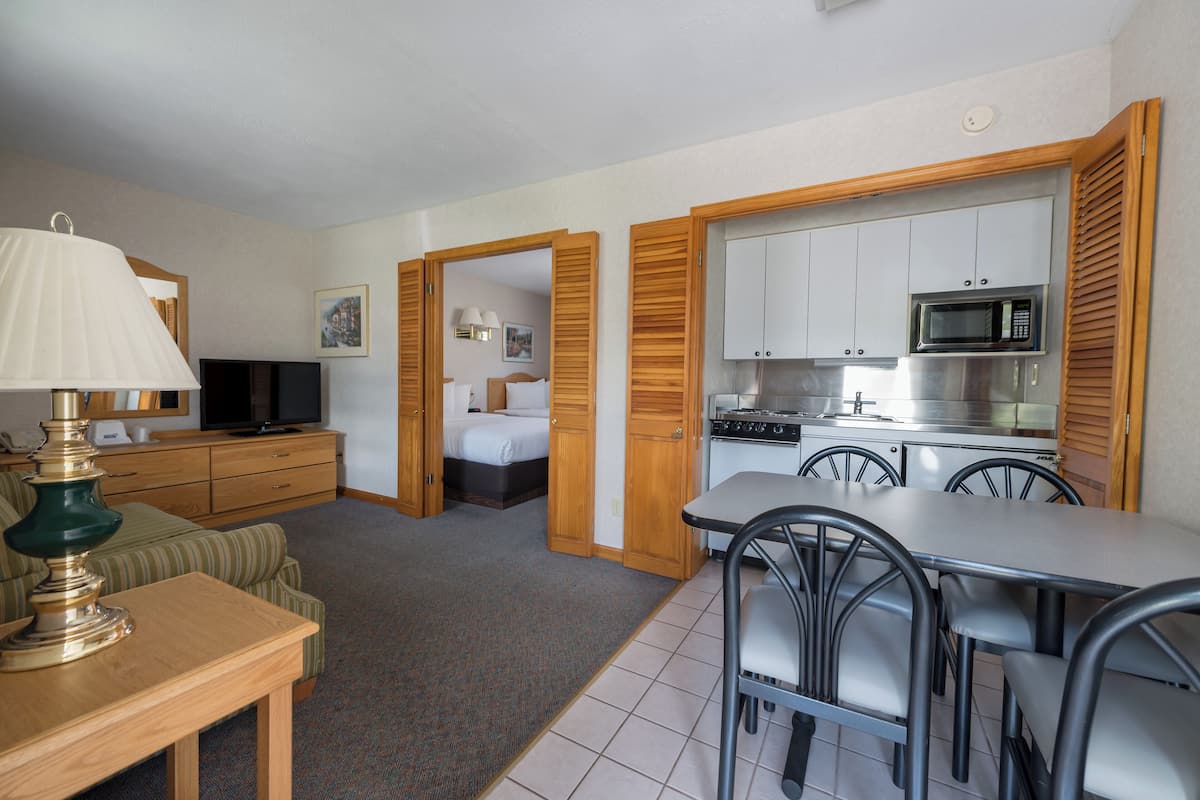 A compact hotel room with a kitchenette, a dining area, a bed, and a TV.