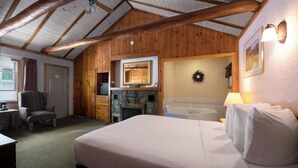 Une pièce chaleureuse avec un grand lit, une cheminée, un mur en pierre et des poutres en bois au plafond.