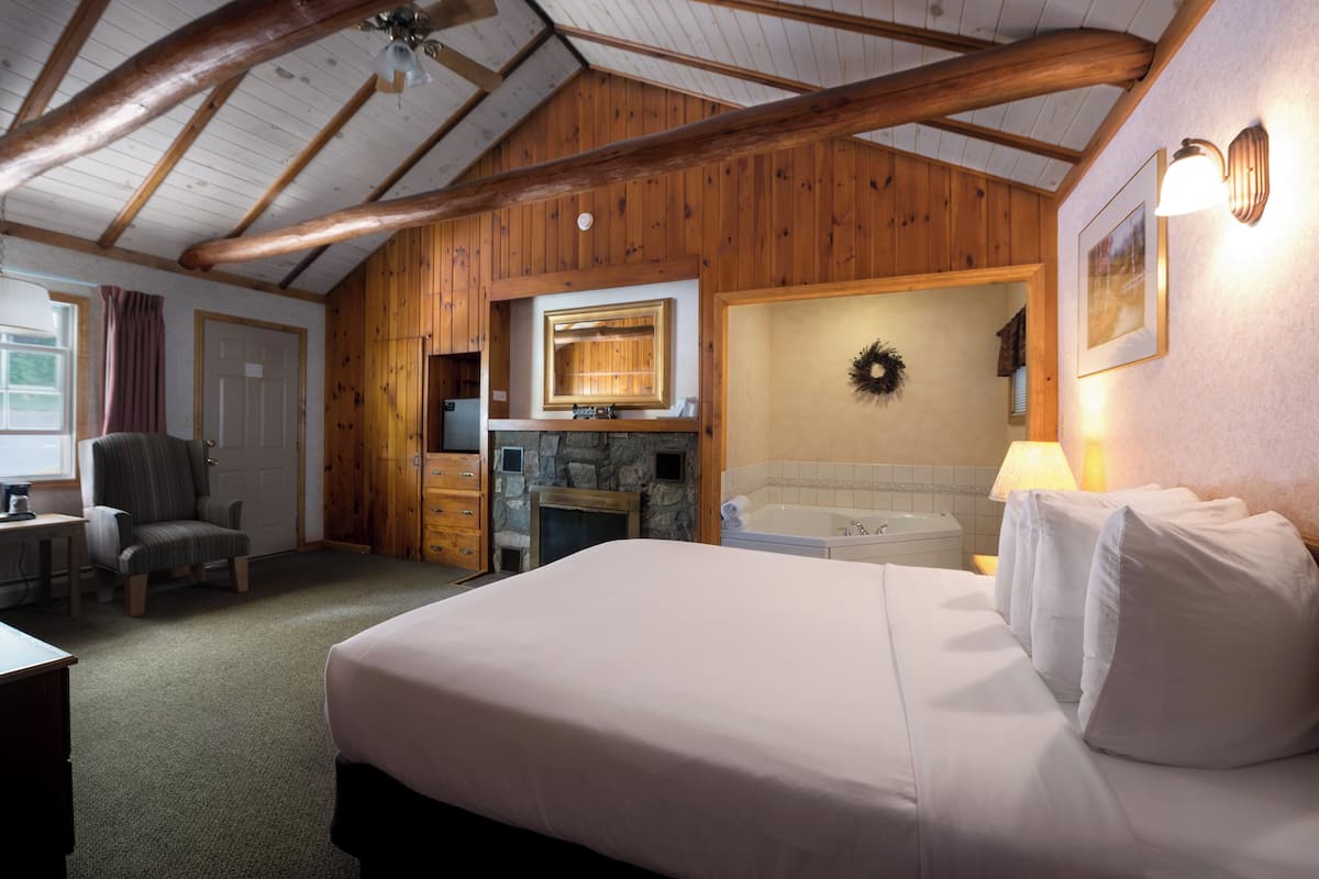 A cozy room with a large bed, a fireplace, a stone wall, and wooden beams on the ceiling.