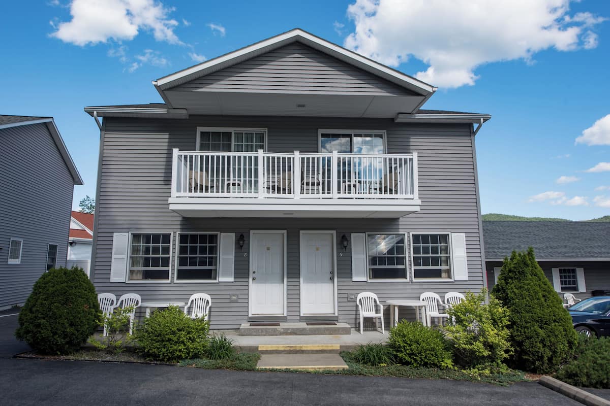 A two-story building with a balcony, white doors, and a small porch area with white chairs.
