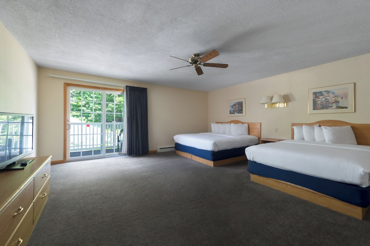 A hotel room with two beds, a ceiling fan, a TV, and a view of the outdoors.