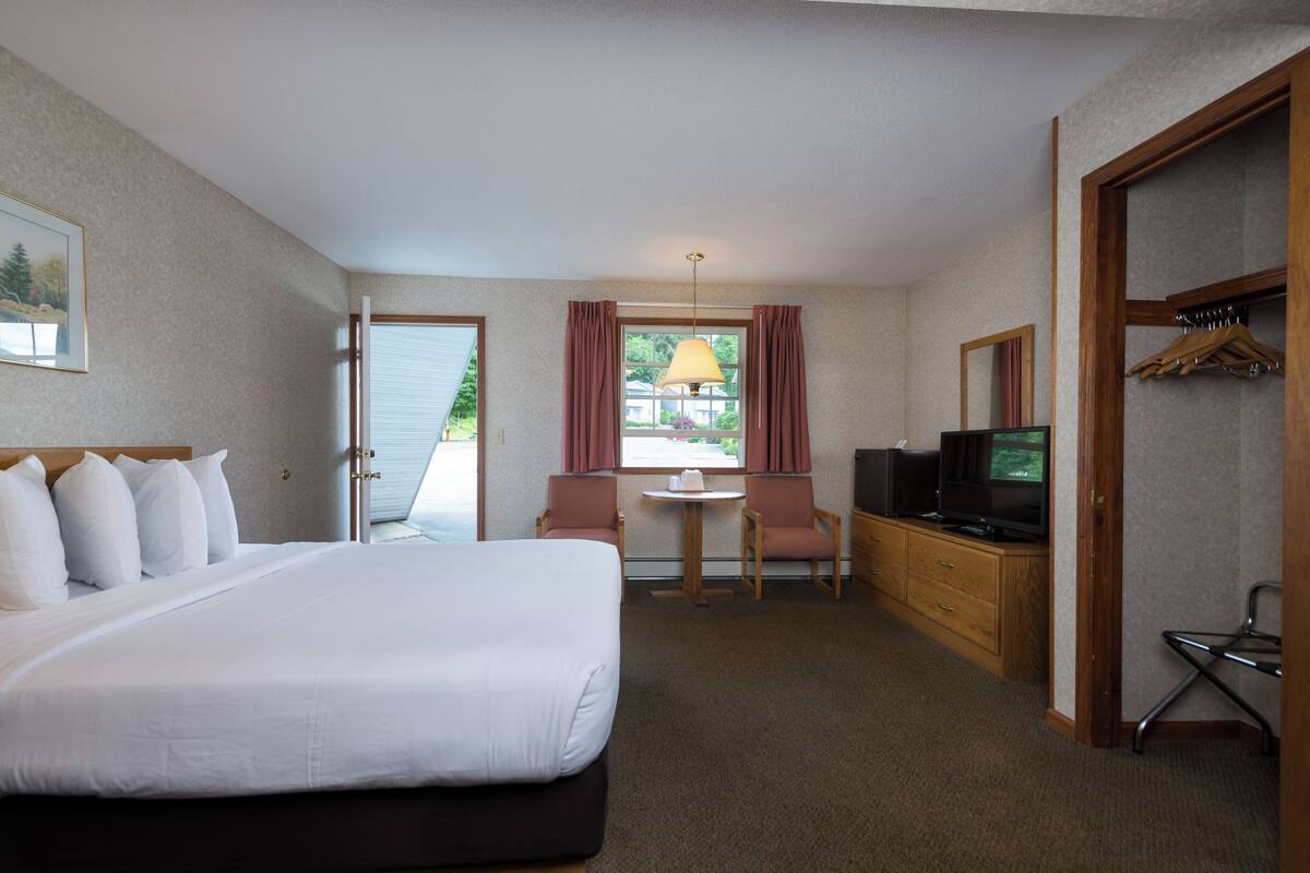 A hotel room with a large bed, a desk with a television, a chair, and a small table.