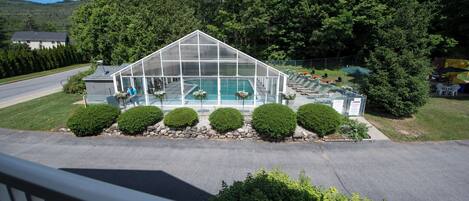 A large greenhouse-style structure with a swimming pool, surrounded by well-maintained bushes and a paved area.