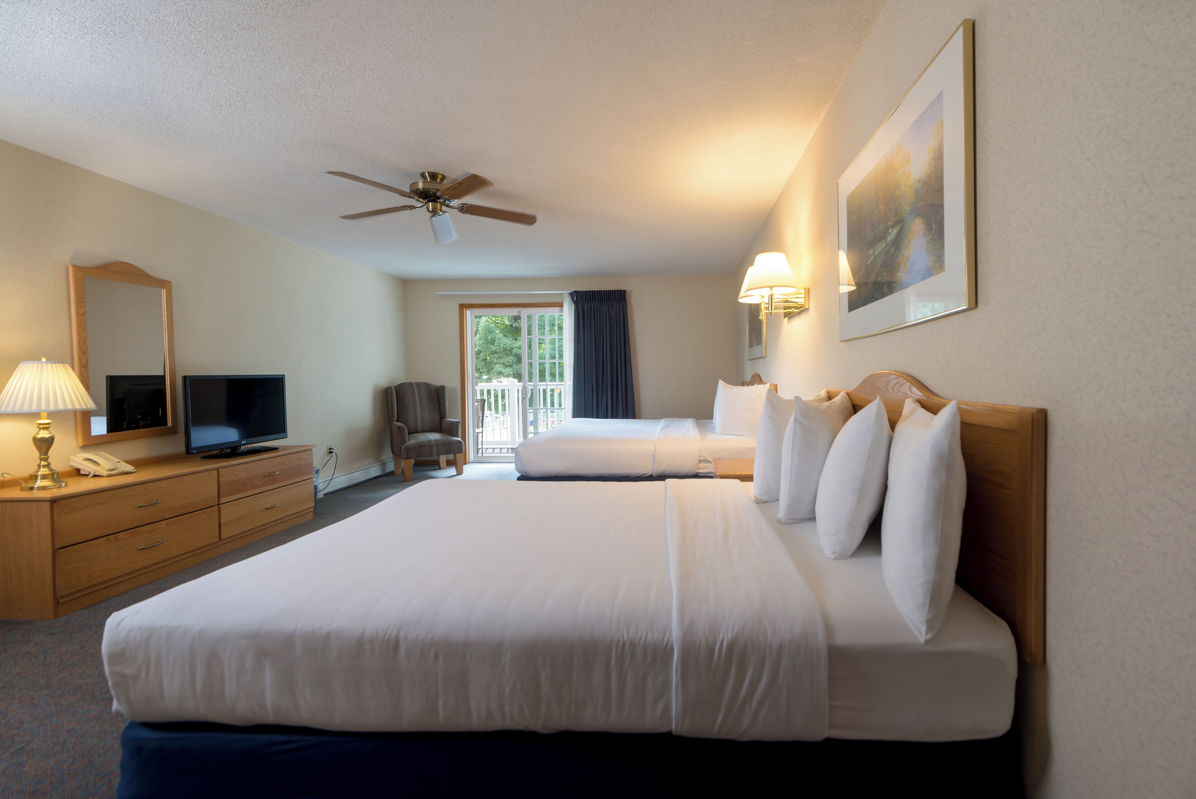 A hotel room with a large bed, a desk with a lamp, a television, and a ceiling fan.