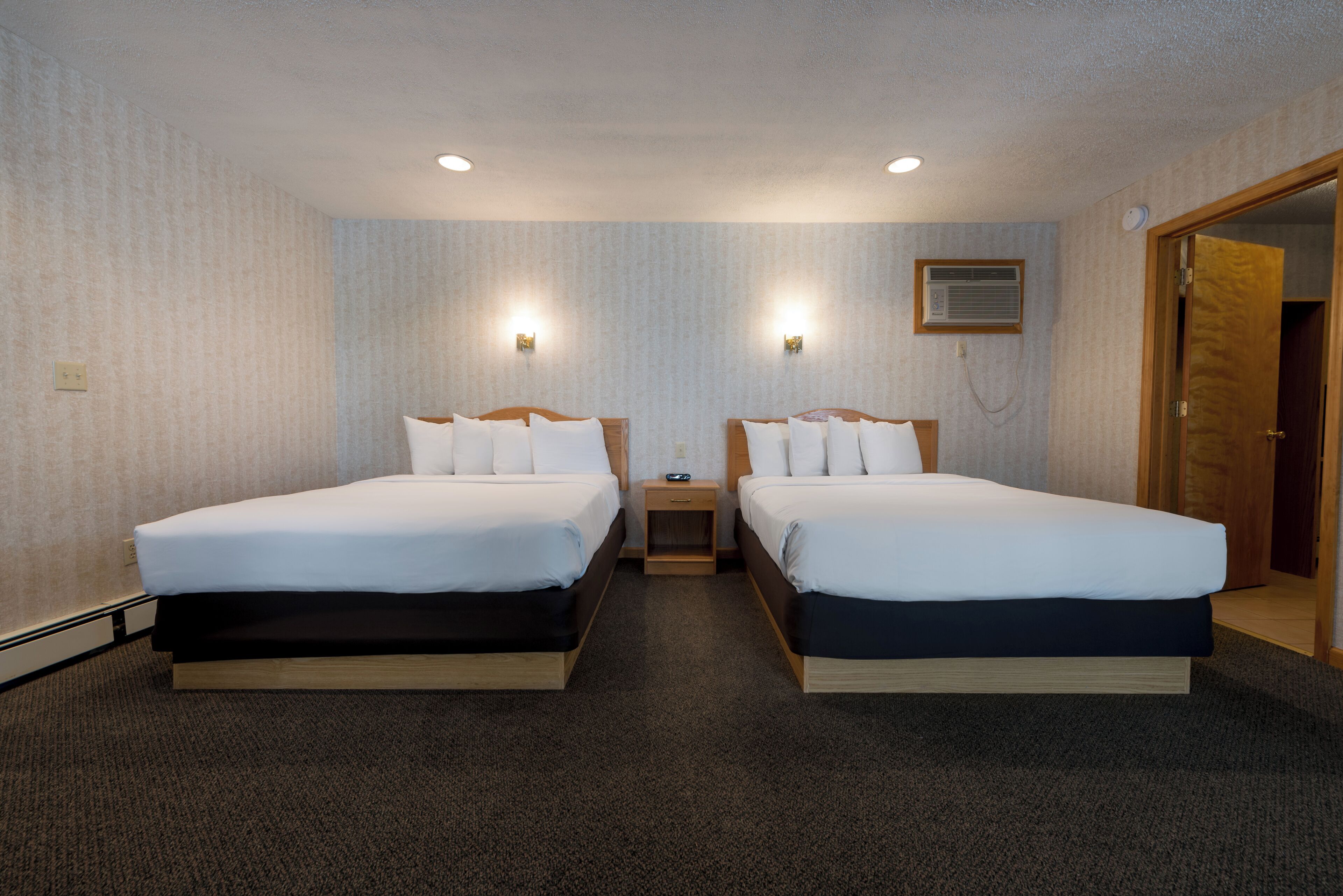 Une chambre d’hôtel avec deux lits, un sol recouvert de moquette et une petite table de chevet avec une lampe.