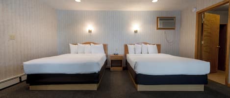 Une chambre d’hôtel avec deux lits, un sol recouvert de moquette et une petite table de chevet avec une lampe.