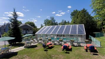 A glass greenhouse with solar panels, outdoor seating, and a pool.