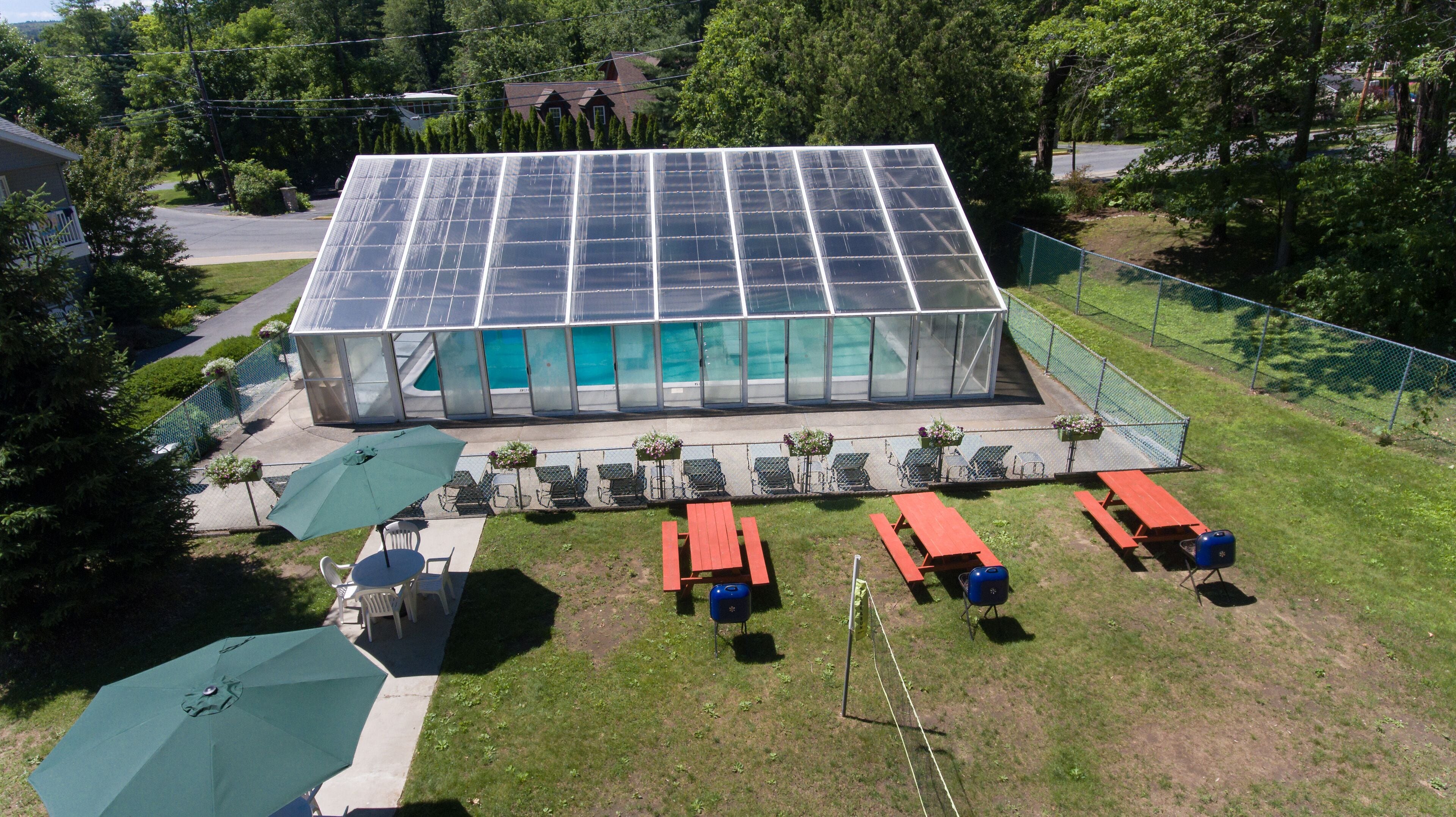 Un edificio con paredes de vidrio, piscina, mobiliario exterior y mesas de picnic.
