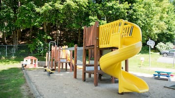 Explore the playground with a spiral slide and climbing frame, set amidst a sandy area surrounded by trees.