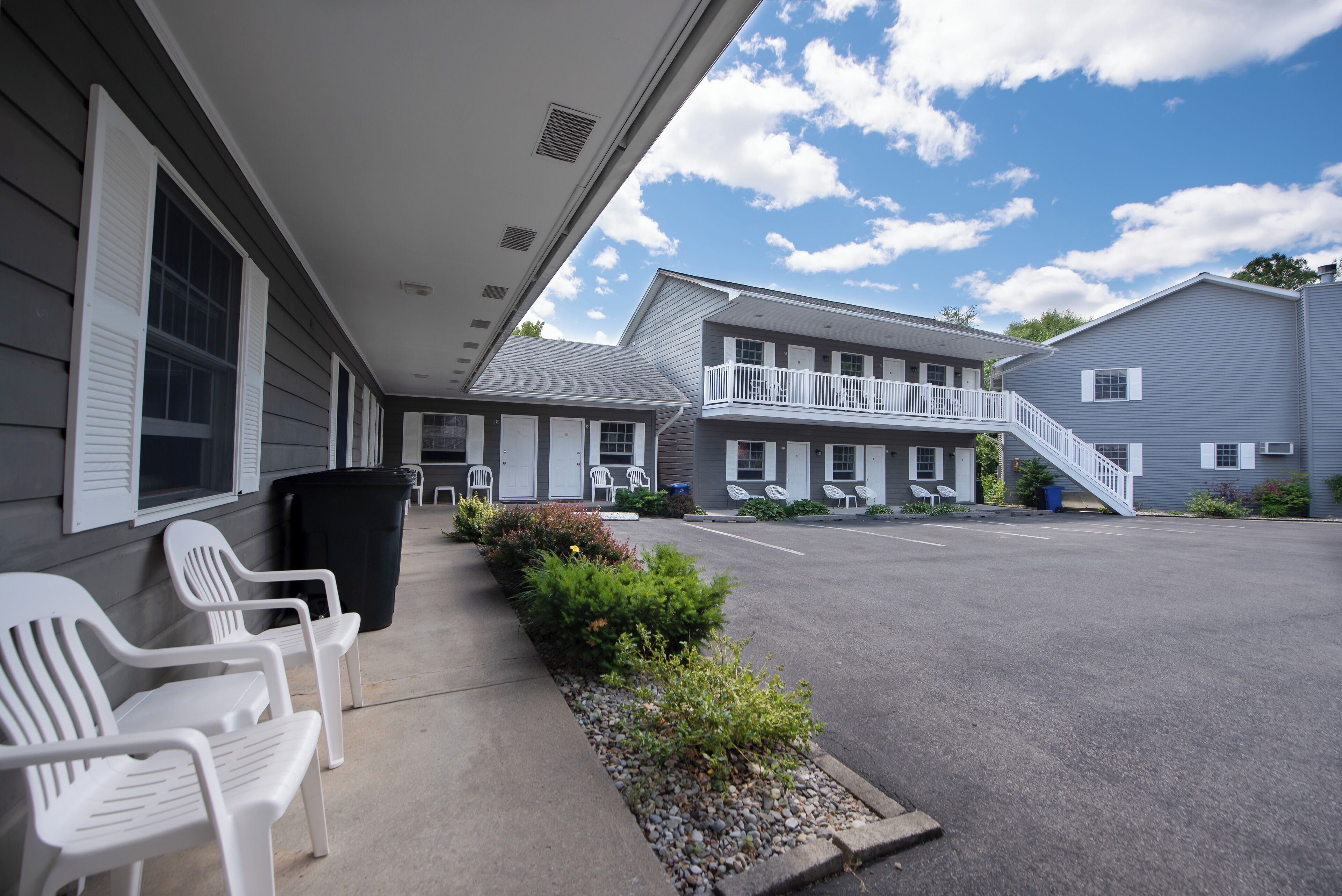 Un motel con área de estacionamiento techada, mobiliario exterior y una escalera que lleva a un nivel superior.
