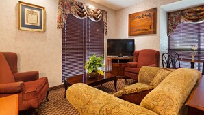 A living room with a television, red chairs, a sofa, and a decorative plaque on the wall. - Best Western Home Place Inn (Camden)