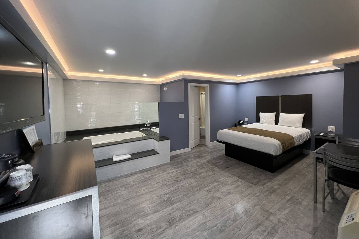 A modern hotel room with a large bed, a separate bathroom with a bathtub, a desk with a chair, and a flat-screen TV.