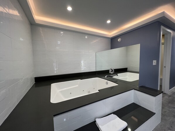 A modern bathroom with a large white bathtub, black countertops, and a mirror above the sink.