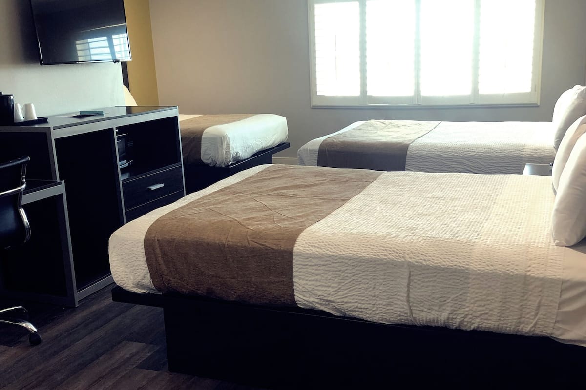 A hotel room with a large bed, a desk with a chair, a TV, and a window with blinds.