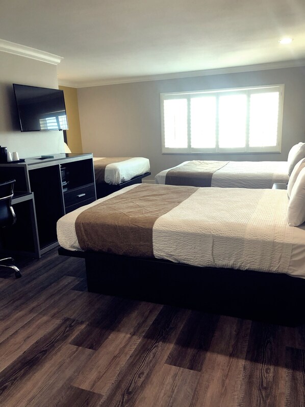 Habitación de hotel con una cama grande, un escritorio con silla, televisor y ventana con persianas.
