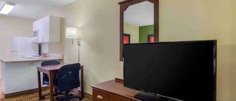 A hotel room with a kitchenette, a desk with a chair, a television on a dresser, and a mirror on the wall.