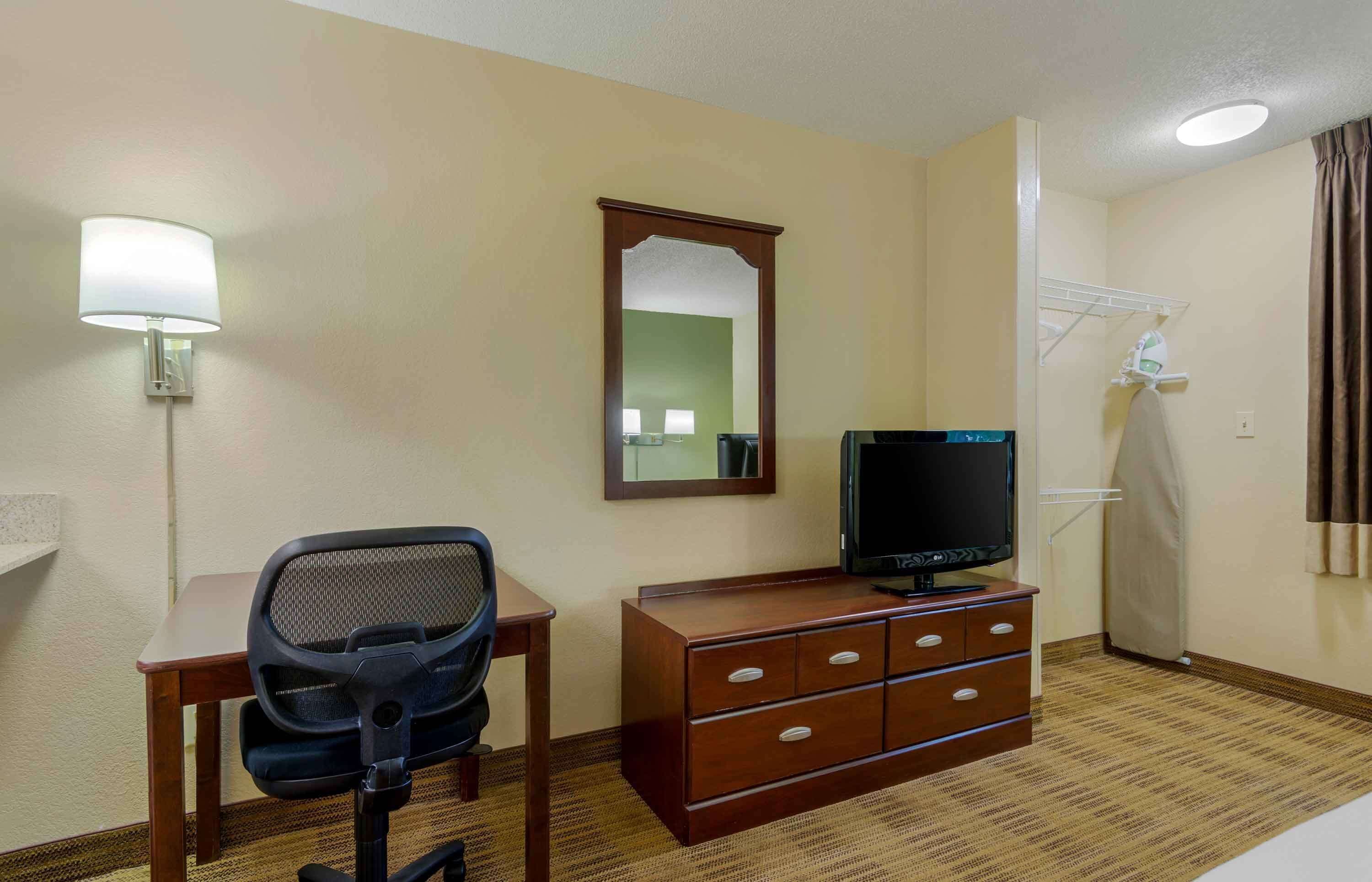 Una habitación de hotel con escritorio, silla, televisión, cómoda, espejo y zona de ducha.