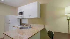 Une cuisine compacte avec des meubles blancs, un four à micro-ondes, un évier et un coin repas comprenant une table et une chaise.