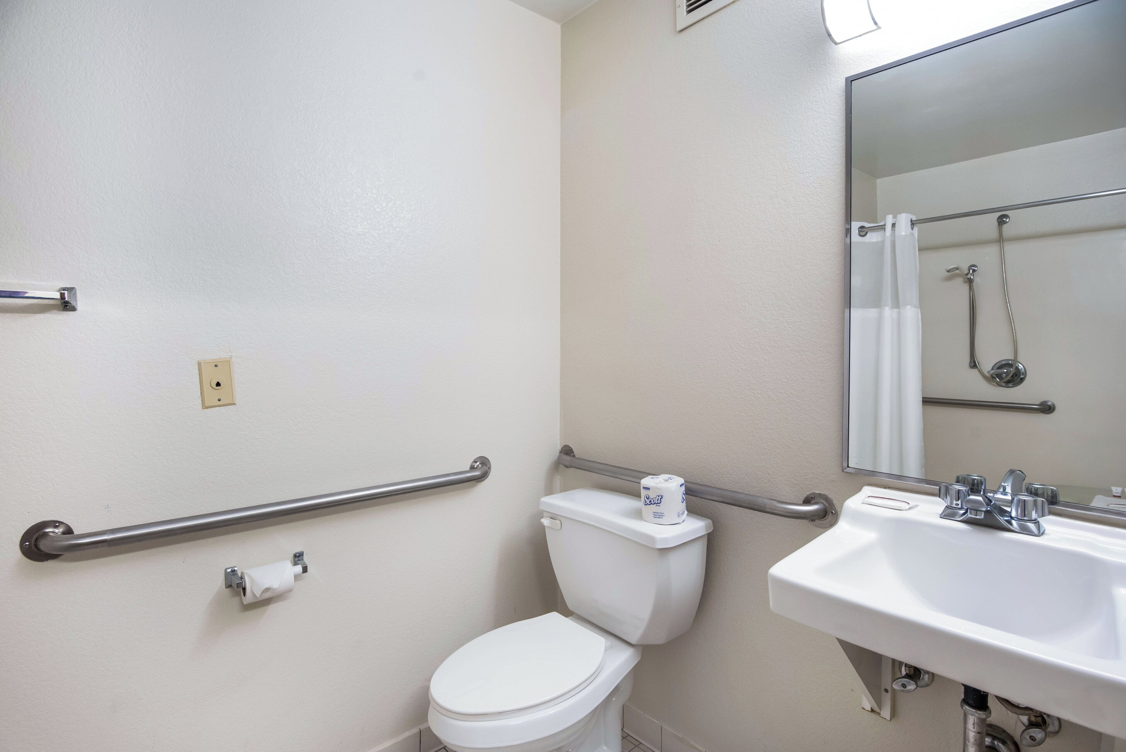A bathroom with a white toilet, a sink, a mirror, and a shower.