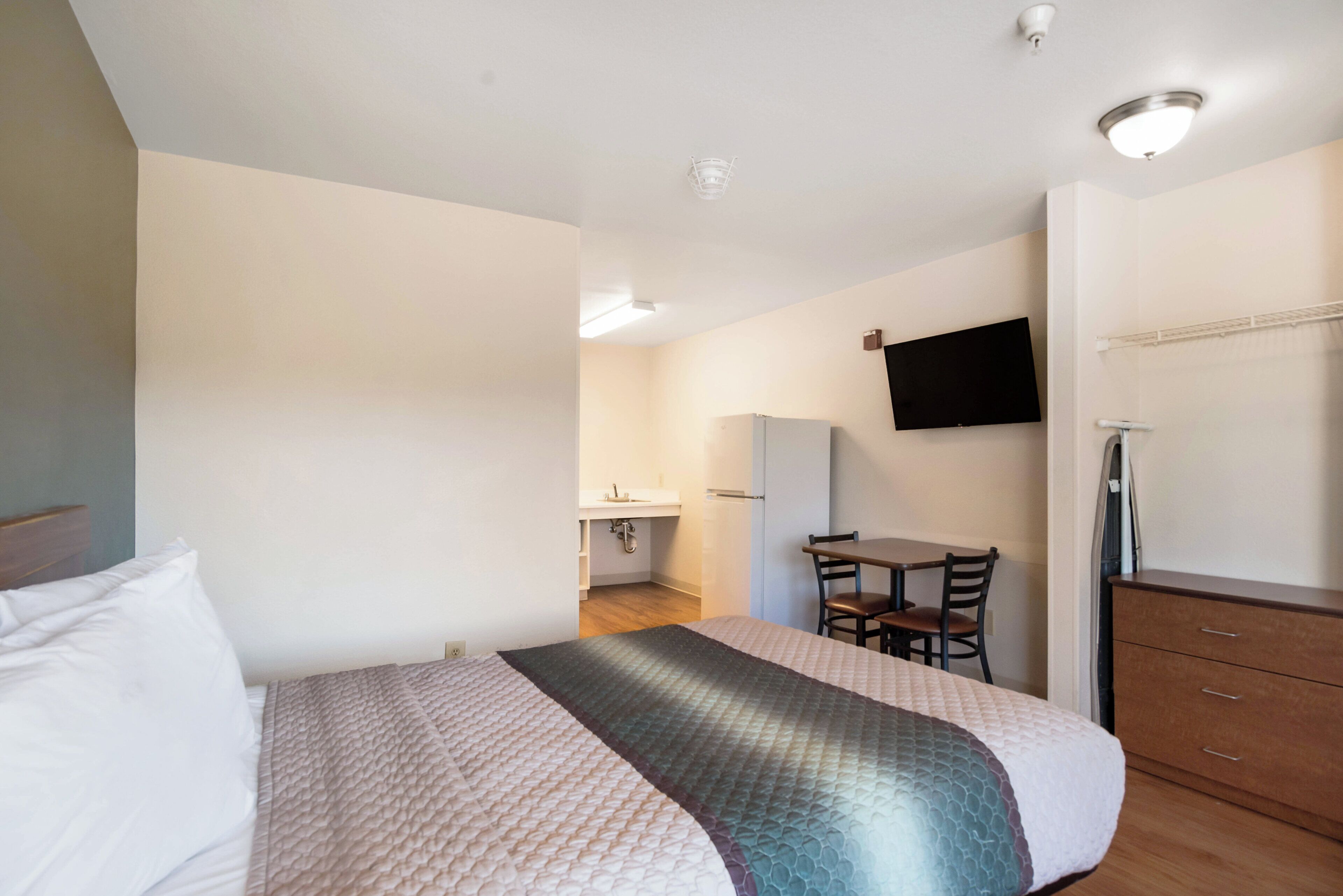 A hotel room with a bed, a desk, a chair, a television mounted on the wall, and a wardrobe.