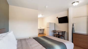 Habitación de hotel con cama, escritorio, silla, televisor montado en la pared y armario.