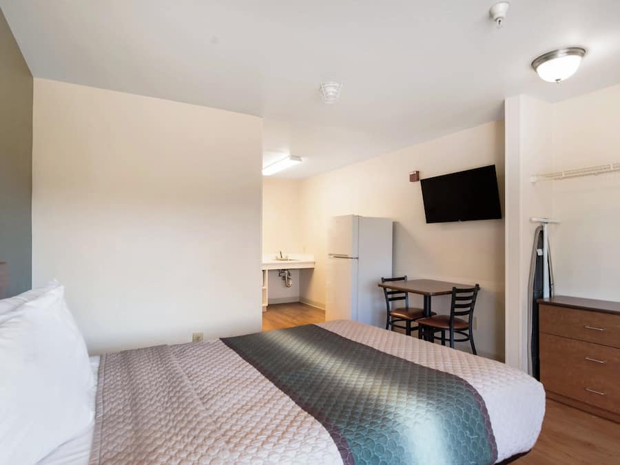 A hotel room with a bed, a desk, a chair, a television mounted on the wall, and a wardrobe.