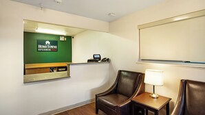 A hotel room with a reception desk, a telephone, a lamp, and two leather chairs. - HomeTowne Studios By Red Roof Colorado Springs - Airport (Colorado Springs)