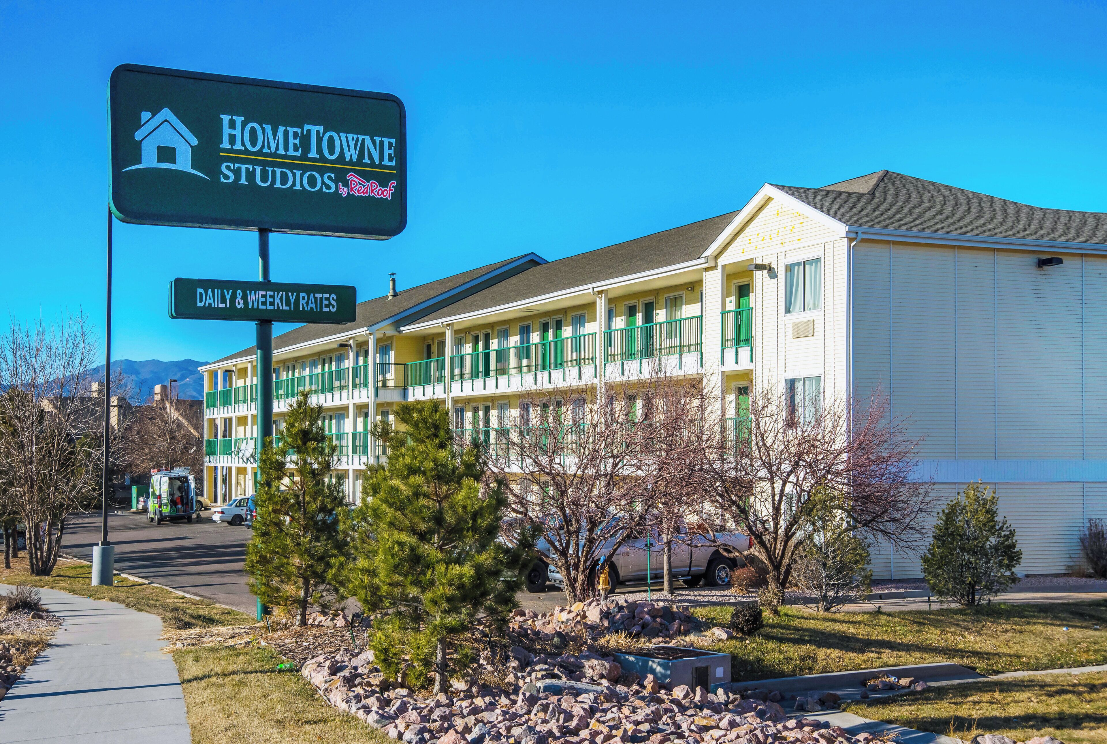 Ein mehrstöckiges Hotel mit einem Schild für 'Home Town Studios by RealKoot' und einem Schild mit der Aufschrift 'Tages- und Wochenpreise'.