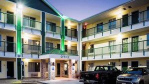 A multi-story hotel with a central office entrance, multiple balconies, and a parking area with two vehicles. - HomeTowne Studios By Red Roof Colorado Springs - Airport (Colorado Springs)
