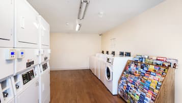 A laundry facility with stacked washing machines, dryers, and a rack of travel brochures.