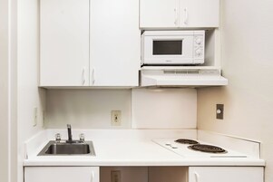 Una kitchenette compacta con microondas integrado, un lavamanos y una placa de cocina.