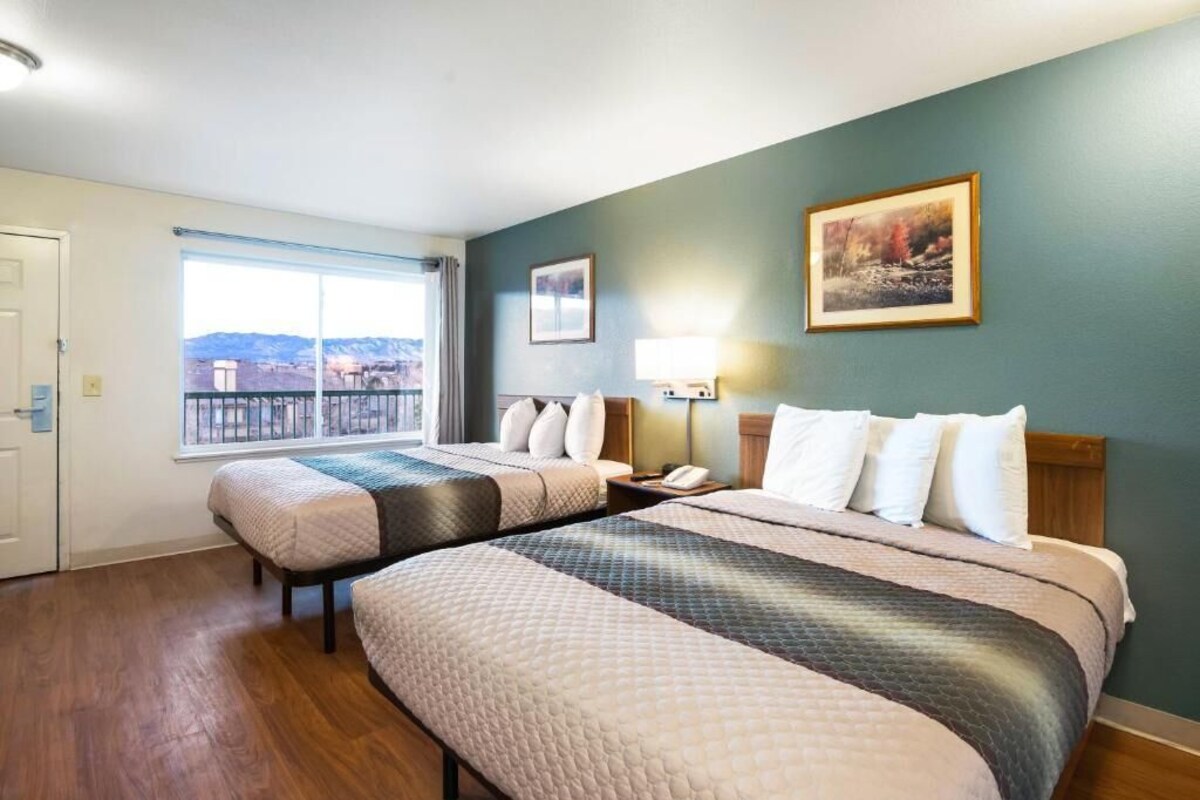 Une chambre d’hôtel avec deux lits, une fenêtre donnant sur un beau paysage, un tableau accroché au mur et une table de chevet avec une lampe.