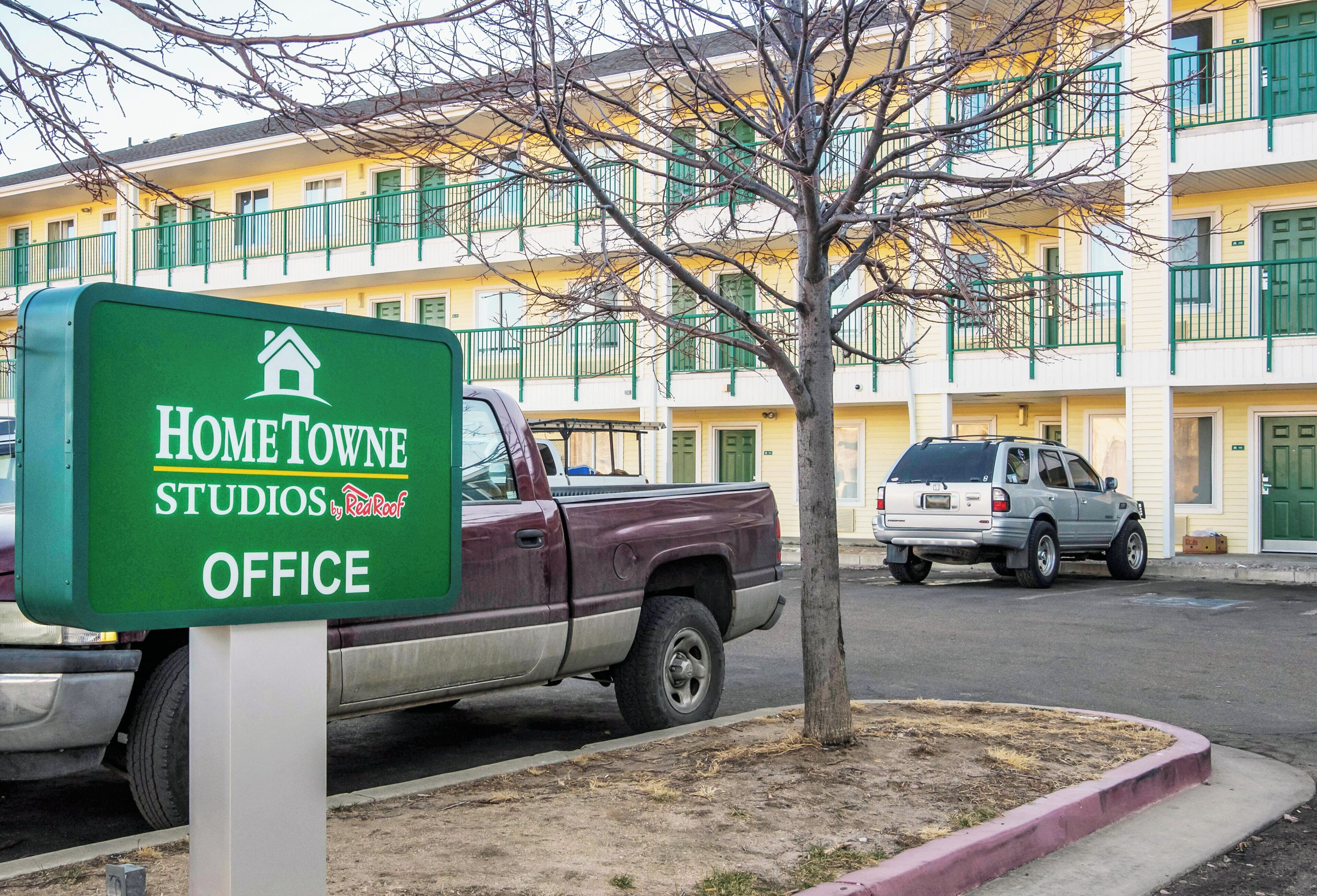 Señalización de HomeTowne Studios Office, con una camioneta estacionada y un edificio al fondo.
