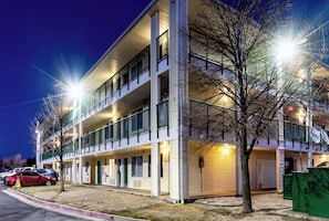 A multi-story hotel with a flat facade, balconies, and a parking area with cars.