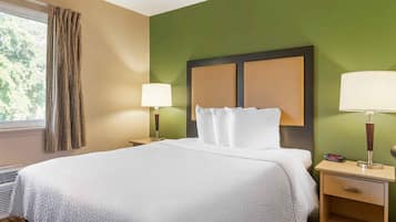 Une chambre d’hôtel avec un grand lit, deux tables de chevet avec des lampes, une fenêtre avec des rideaux et un mur vert.