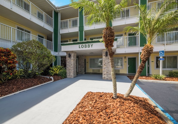 A multi-story hotel with a 'Lobby' sign, outdoor palm trees, and a parking sign indicating accessible parking. - HomeTowne Studios by Red Roof Orlando - UCF Area (Orlando)