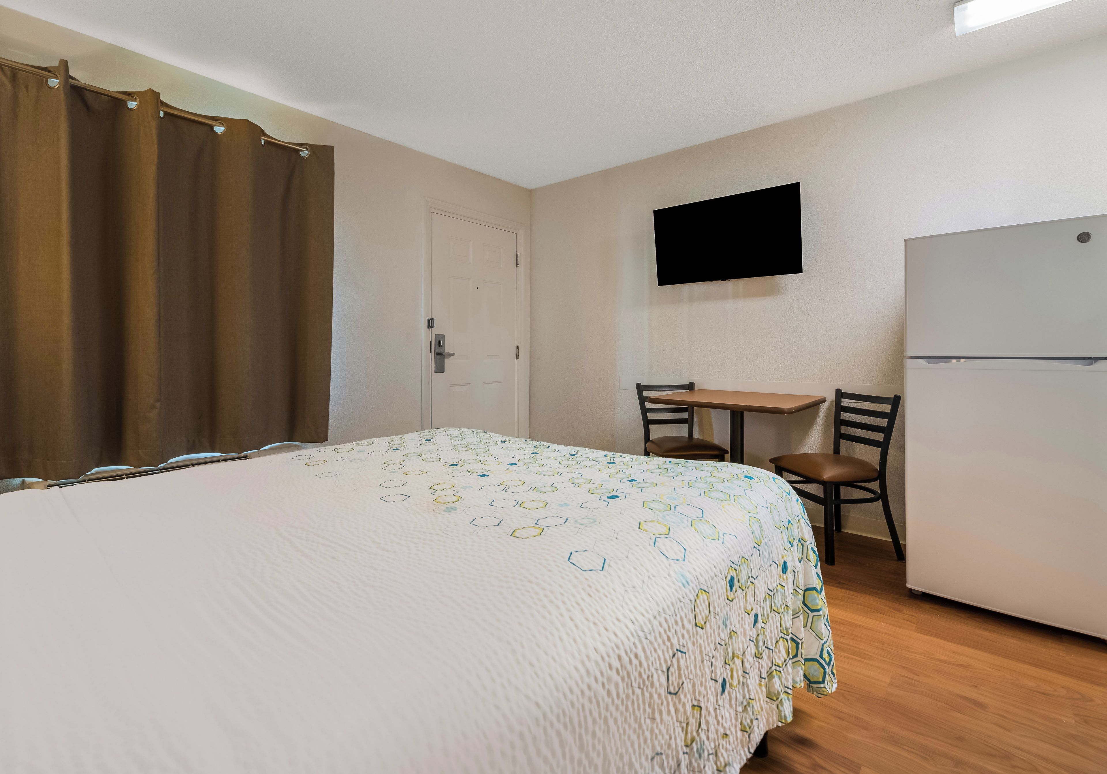 A bedroom with a bed, a desk, a chair, a television, and a refrigerator.