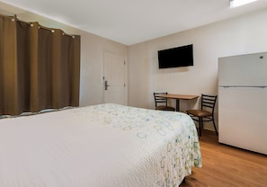 Un dormitorio con cama, escritorio, silla, televisor y refrigerador.