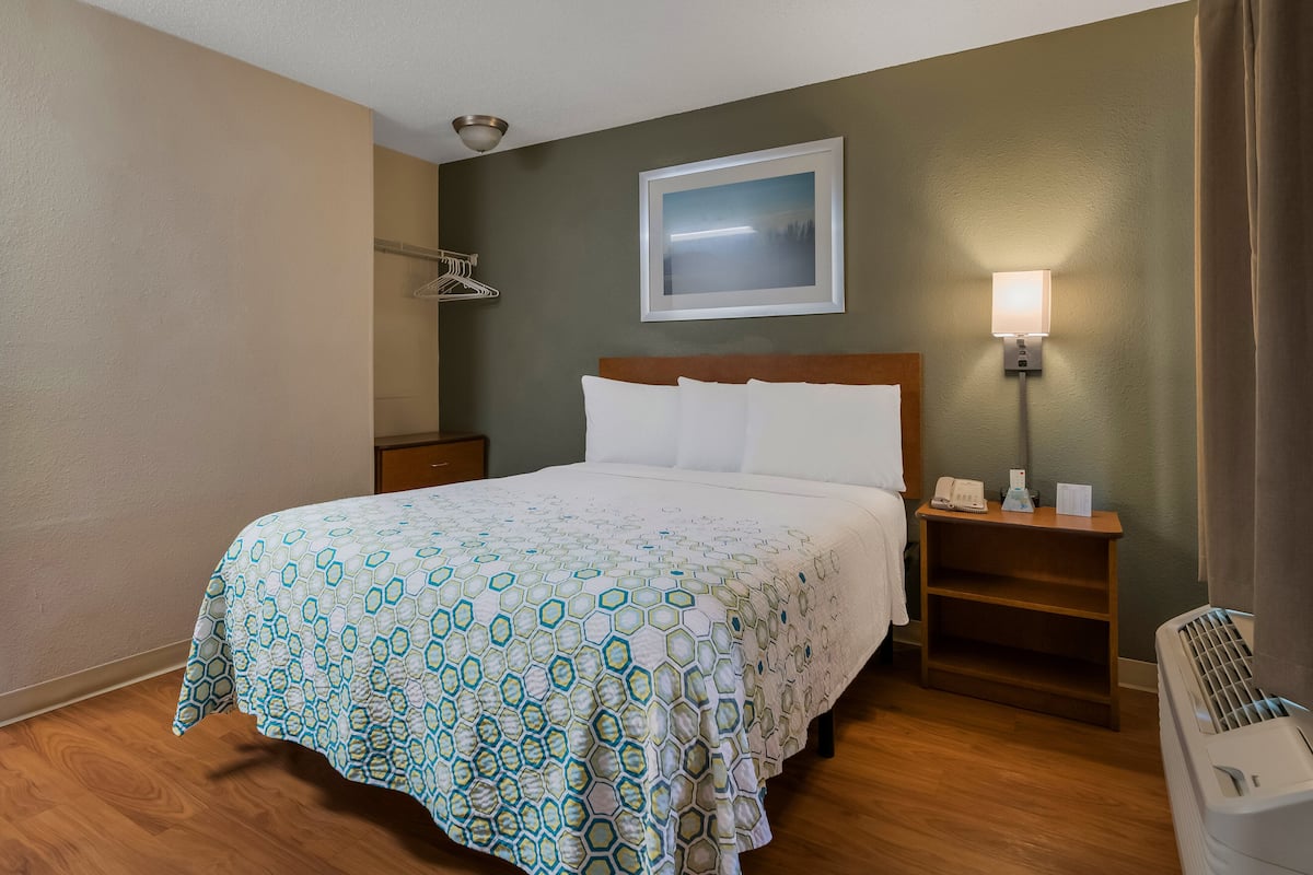 A hotel room with a bed, a nightstand, a lamp, and a heater.