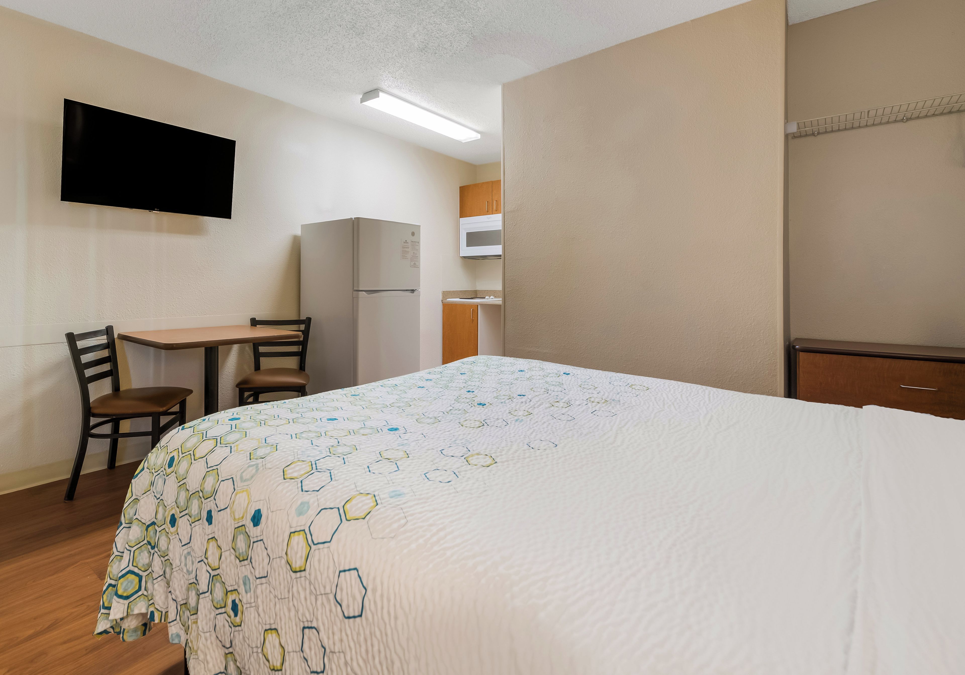 Habitación de hotel con cama, escritorio, silla, televisor, refrigerador y microondas.